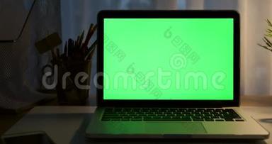 带有绿色屏幕的笔记本电脑。 黑暗的办公室。 多莉向左向右移动。 完美地放置你自己的图像或视频。 技术绿屏